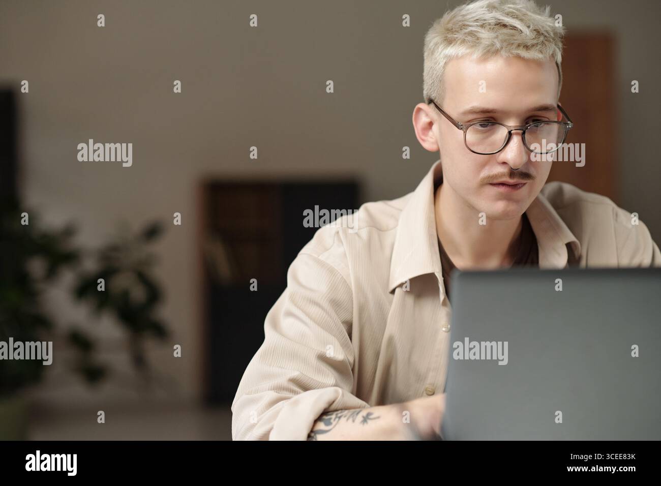 Junger Z-Mann mit Brille, der im modernen Büro am Laptop arbeitet, Kopierraum Stockfoto