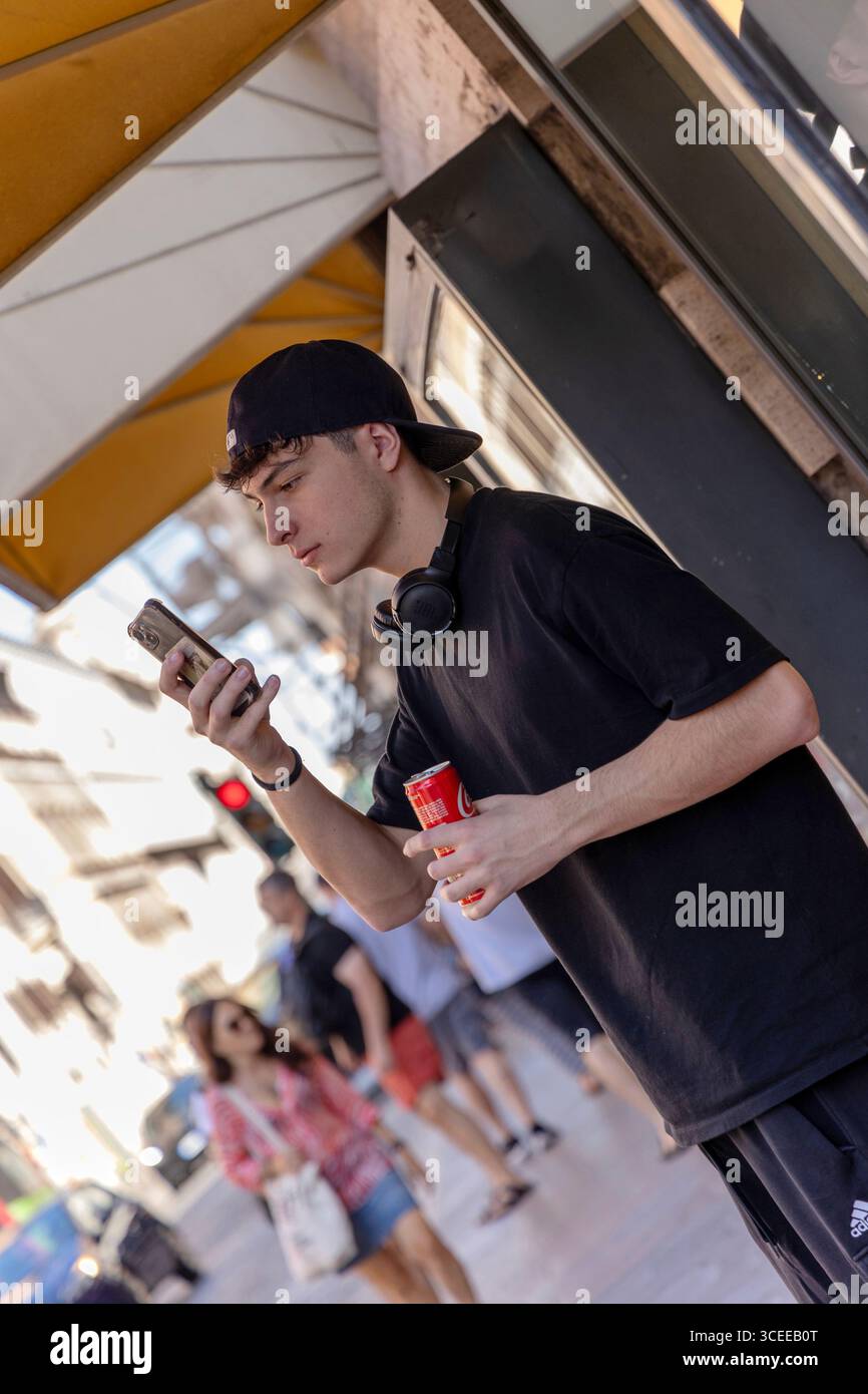 Junger Mann trinkt Cola und benutzt Telefon auf der Straße, Rom, Italien Stockfoto