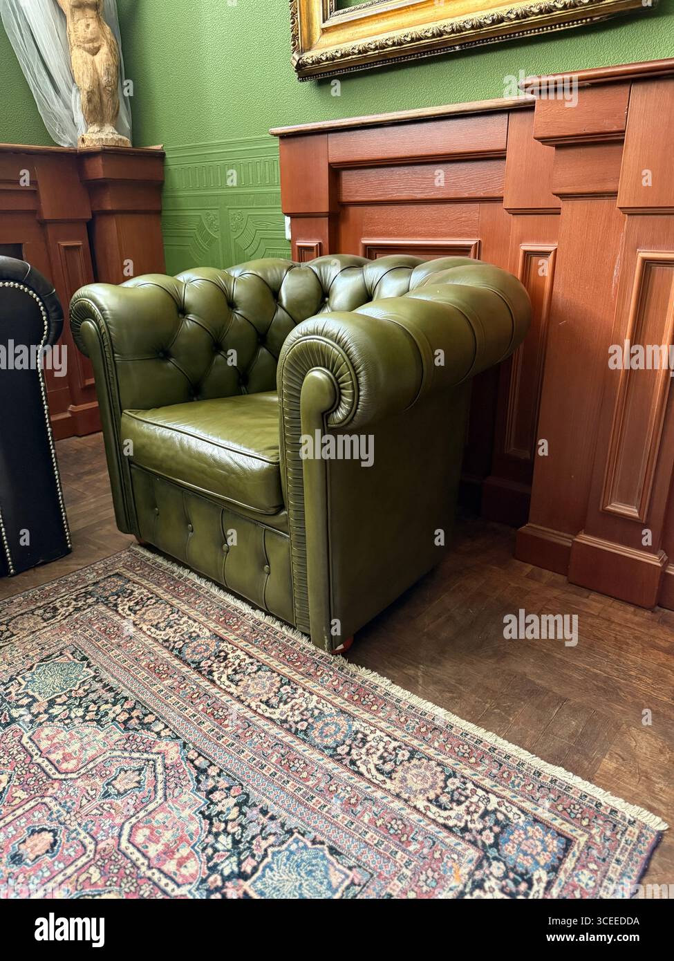 Luxuriöser grüner Ledersessel in Vintage-Zimmer mit kunstvoller Holztäfelung und Teppichhintergrund. Mobiles Foto Stockfoto
