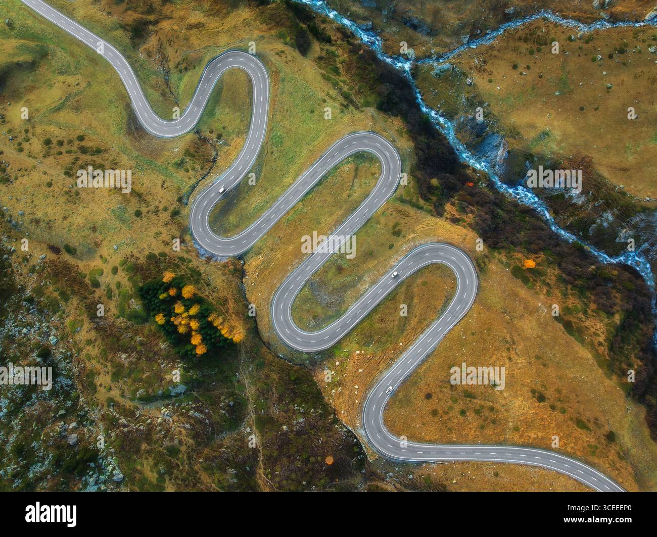 Aus der Vogelperspektive auf die gewundene Bergstraße, den Fluss im alpinen Tal Stockfoto