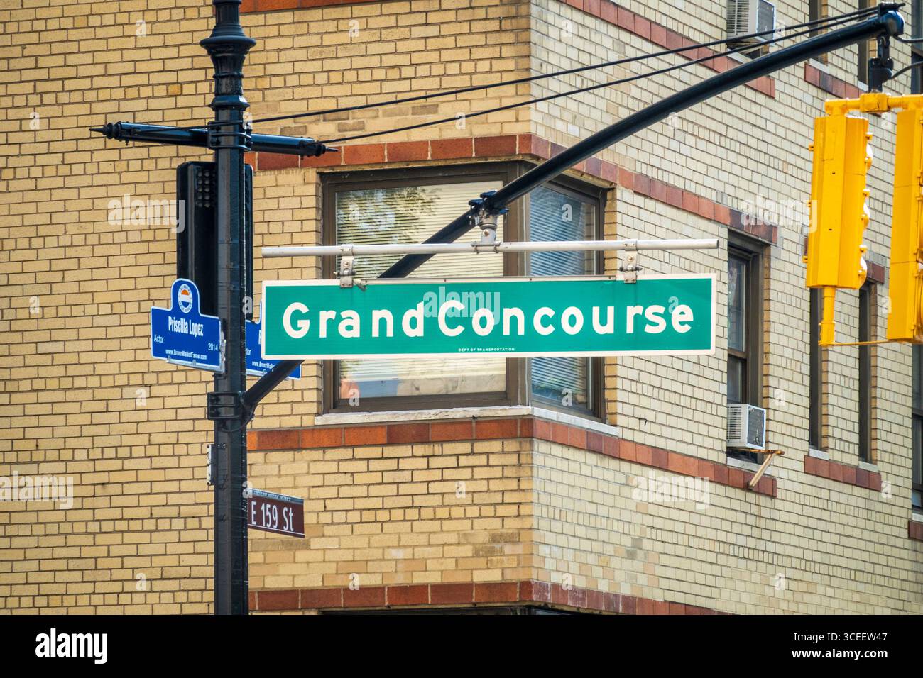 Bronx, NY - USA - 16. August 2025 Ein grünes Straßenschild für Grand Concourse, das sich mit der E 159 St. kreuzt, mit einem kleineren blauen Schild für Priscilla Lopez A Lampe Stockfoto