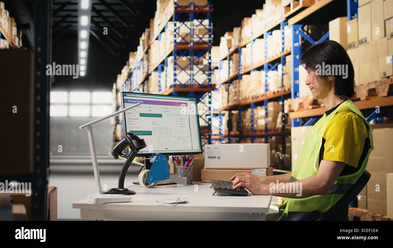 Zwei Kollegen arbeiten an der Auftragsbearbeitung in industriellen Lagerhäusern und tragen Warnwesten in der Nähe von riesigen Lagerregalen. Asiatischer Mann, der die Versanddaten auf dem Computer eingibt. Kamera A.. Stockfoto