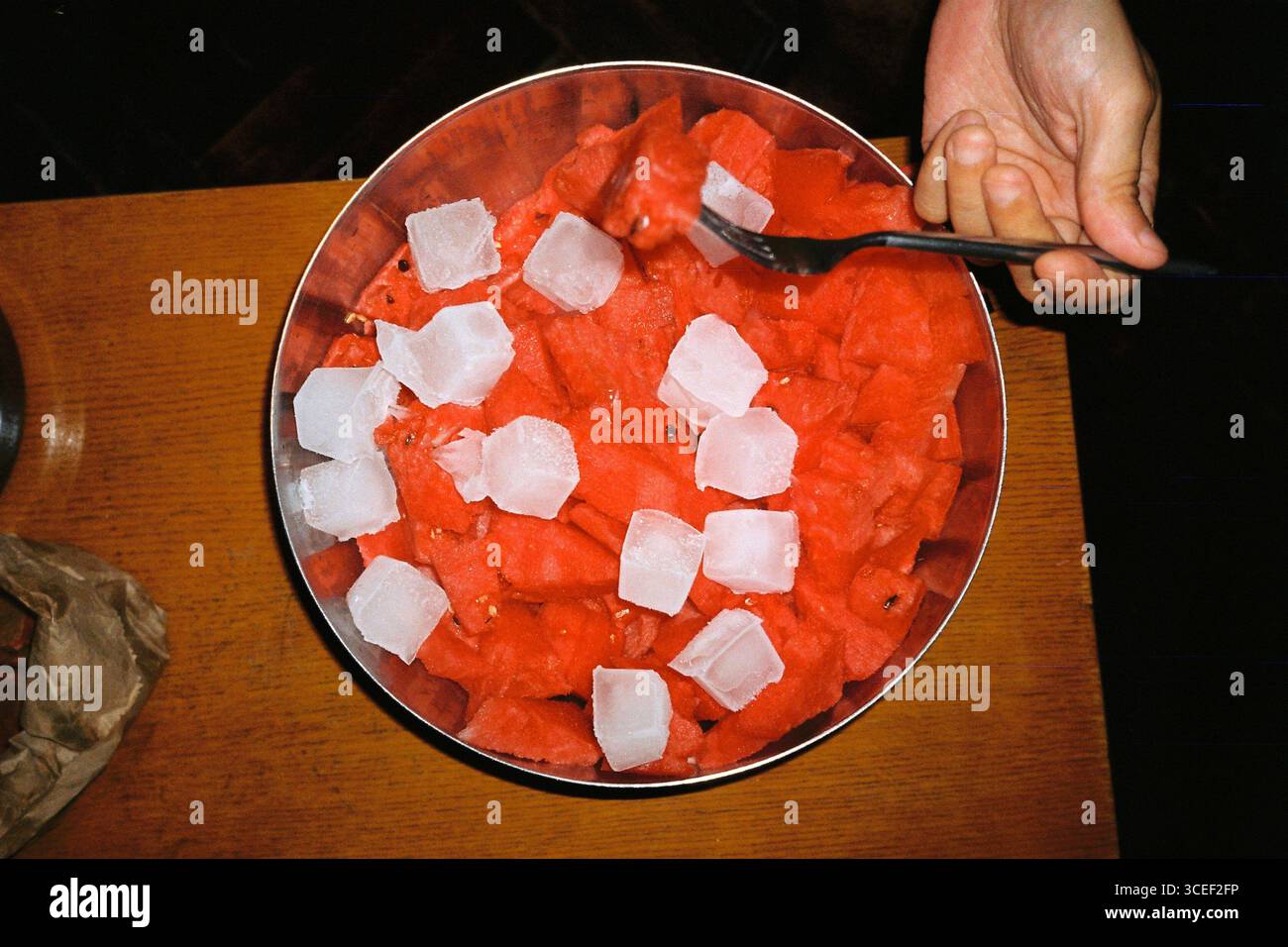 Ein Foto von in Scheiben geschnittener Wassermelone in einer Metallschale mit Eiswürfeln auf der Oberseite, aufgenommen aus einem Überkopfwinkel mit einem Olympus-Mju- und Kodak-Gold-Film und einem ha Stockfoto
