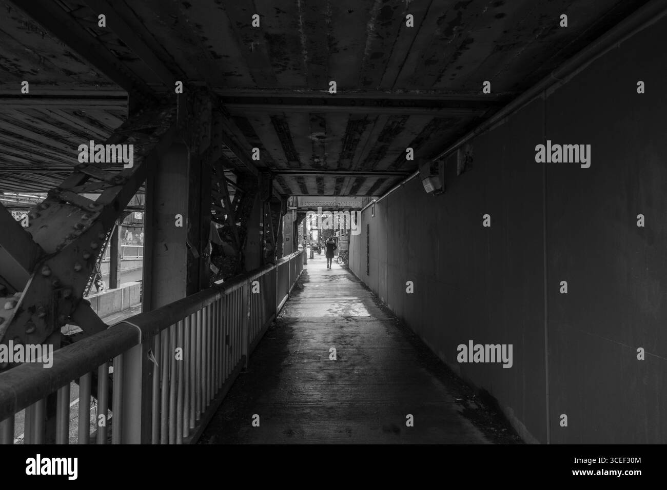 Schwarz-weiß einer unterirdischen Gasse oder unter einer Autobahn mit der Silhouette eines Menschen, der den horizontalen Schwarzweiß-Hintergrund hinter dem Licht verlässt Stockfoto