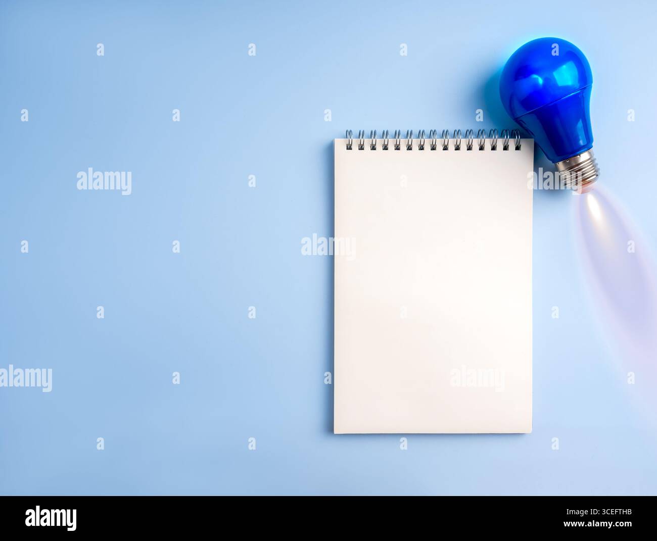 Kreatives Konzept mit blauer Glühbirne als Flugjet und leerem Notizbuch auf blauem Hintergrund mit Raum, symbolisiert Innovation, Ideenplanung, Kreativität Stockfoto