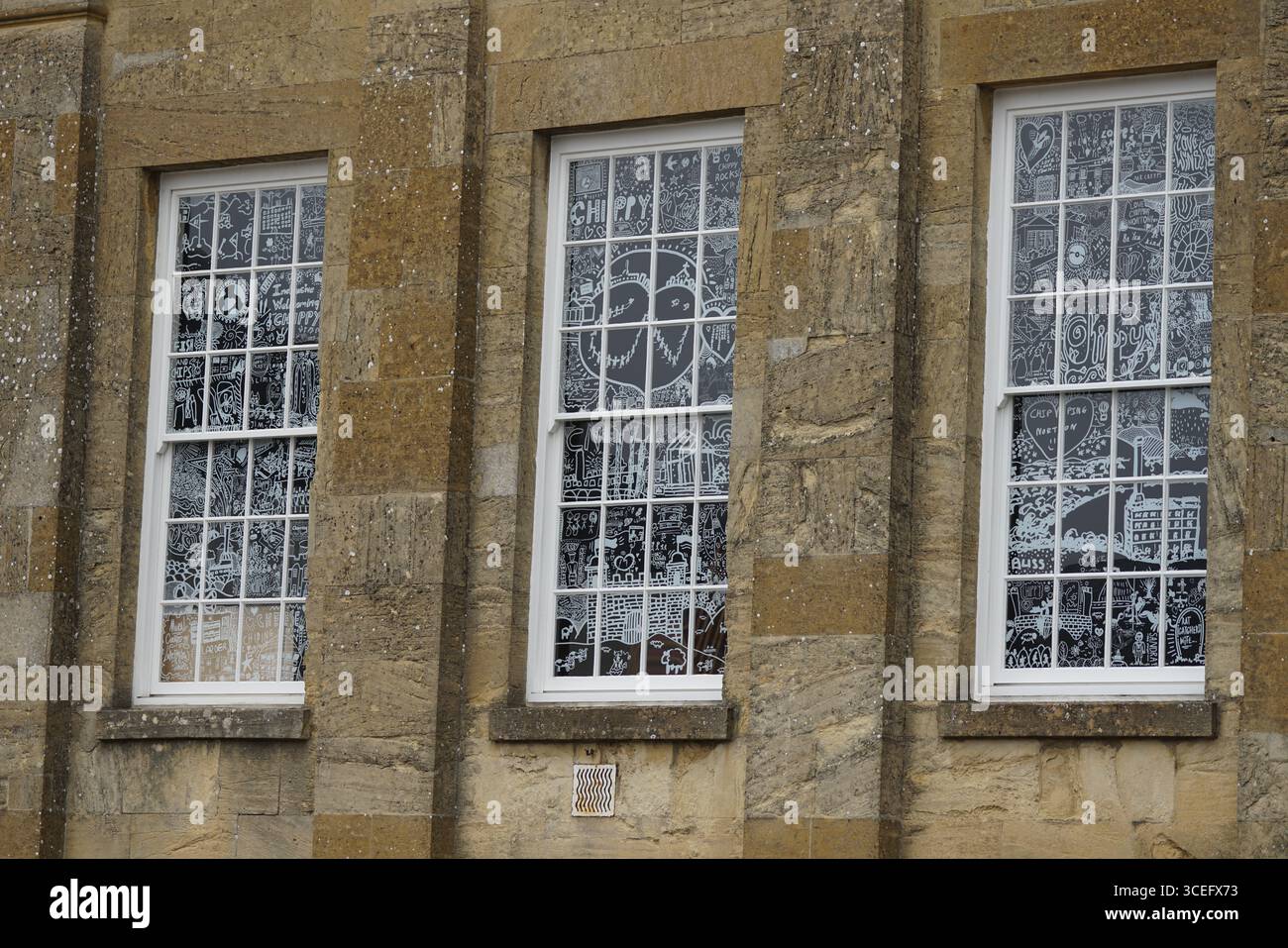 Dekorierte Fenster mit komplexen Kunstwerken auf einem historischen Steingebäude. Chipping Norton, England Stockfoto