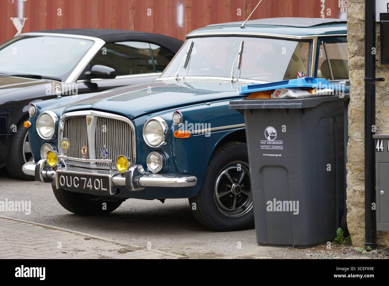 Klassischer blauer Oldtimer, der in der Nähe Eines Recyclingbehälters geparkt ist. Chipping Norton, England Stockfoto