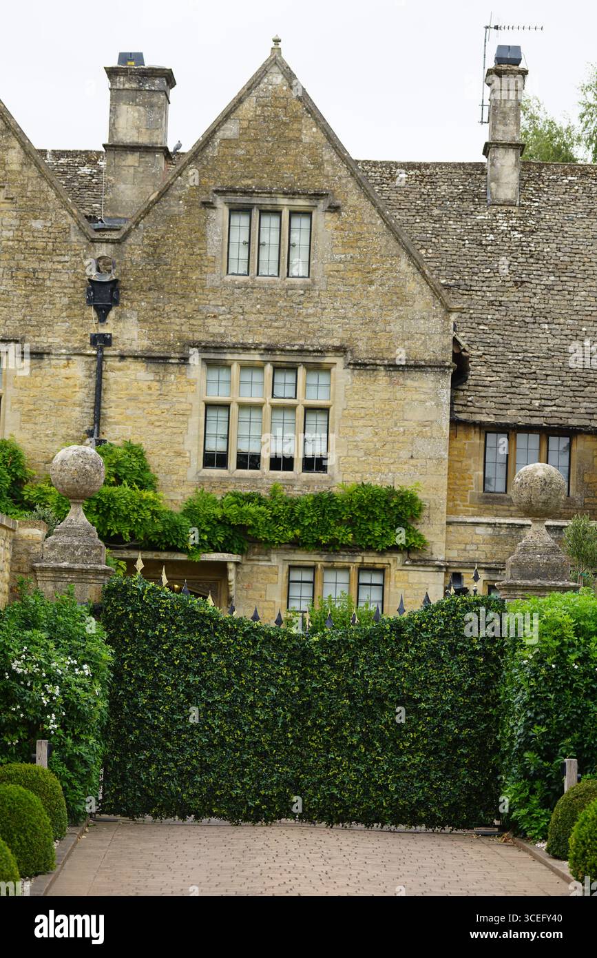 Elegantes historisches Steinhaus mit üppigem Grün und dekorativem Gartentor. Bourton-on-the-Water, England Stockfoto