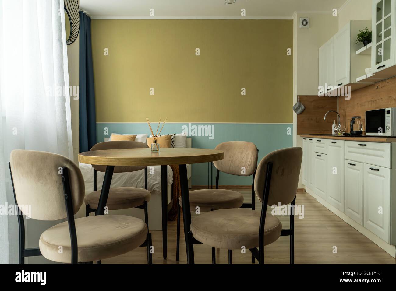 Das Innere eines kleinen Apartments mit Bett, Kissen, hellen Küchenmöbeln, Stühlen mit Tisch, Küchengeräten und Kühlschrank. Das Apartment hat Stockfoto