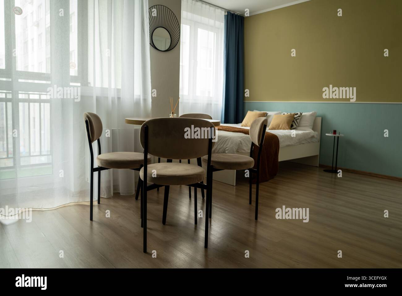 Das Innere eines kleinen Apartments mit Bett, Kissen, hellen Küchenmöbeln, Stühlen mit Tisch, Küchengeräten und Kühlschrank. Das Apartment hat Stockfoto