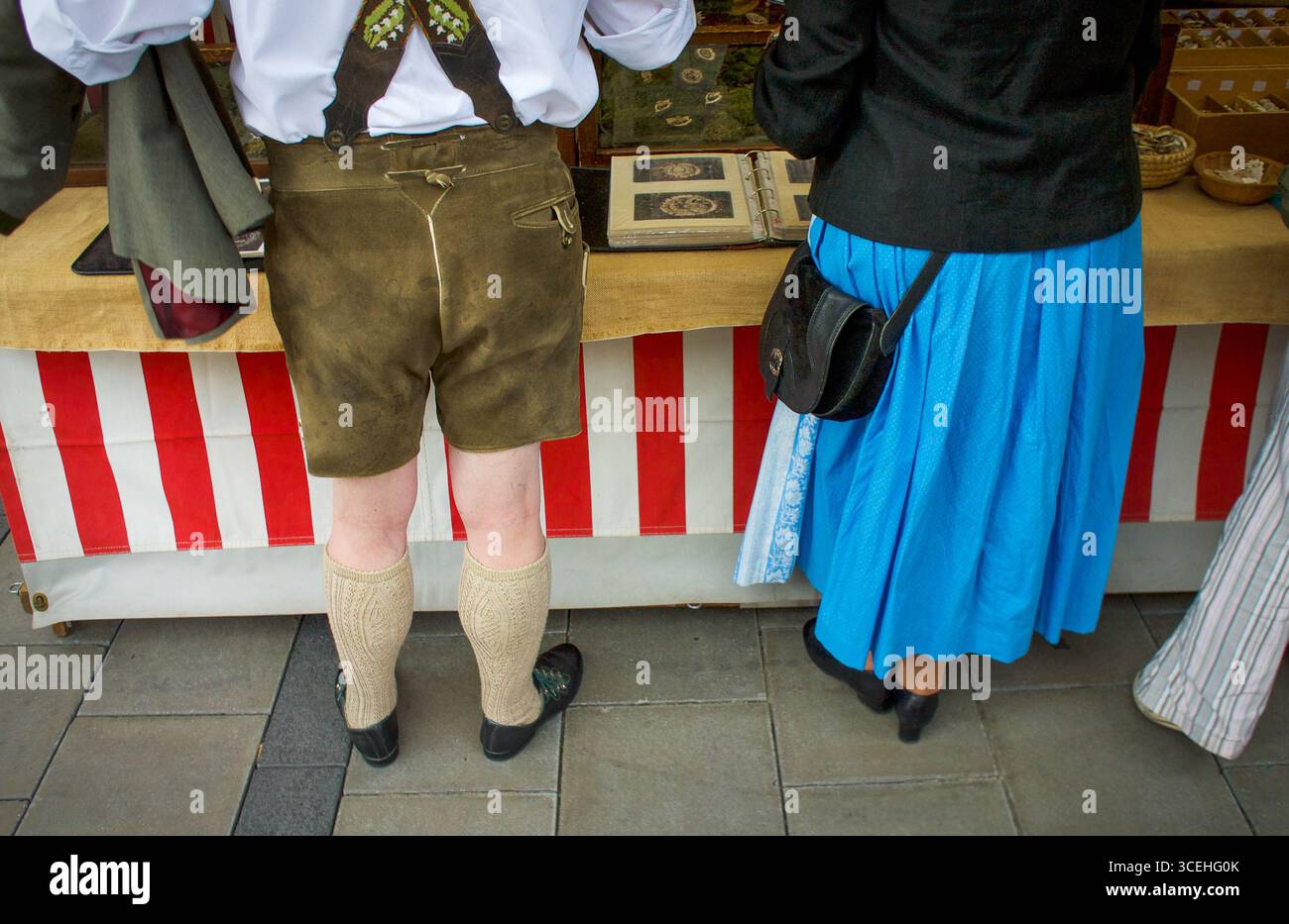 Ein Mann in Lederhose und eine Frau in bayerischer Dirndl-Tracht an einem Marktstand in München. Stockfoto