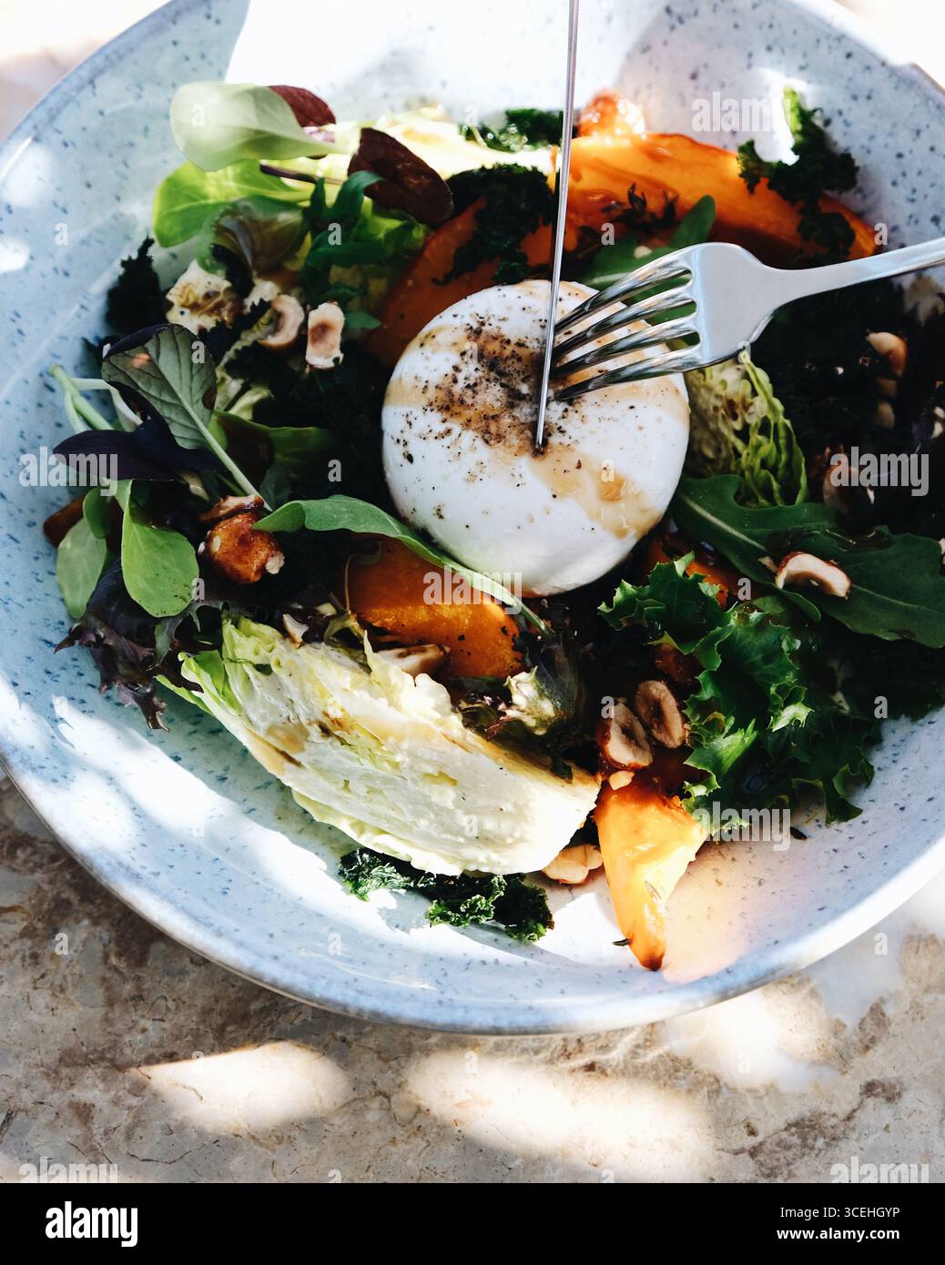 Frischer Burrata-Salat mit gebratenem Kürbis, Blattgemüse, Haselnüssen und Balsamico-Dressing. Gourmet gesunde Gerichte in einer Keramikschale Stockfoto