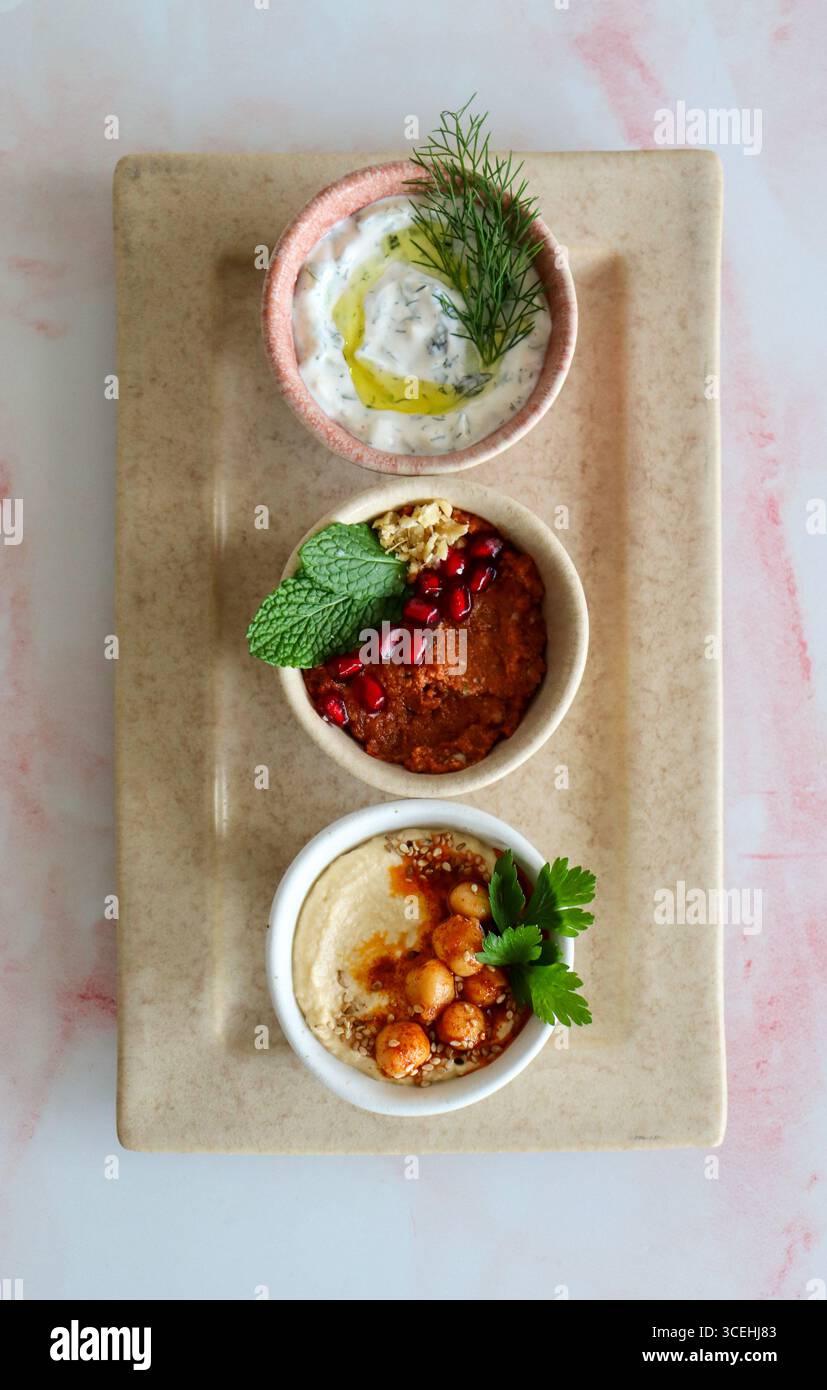 Blick von oben auf eine Platte mit drei Dips, Joghurt-Dip garniert mit Dill und Olivenöl, Tomatenpaste mit Minze und Hummus mit Kichererbsen. Neutralstellung Stockfoto