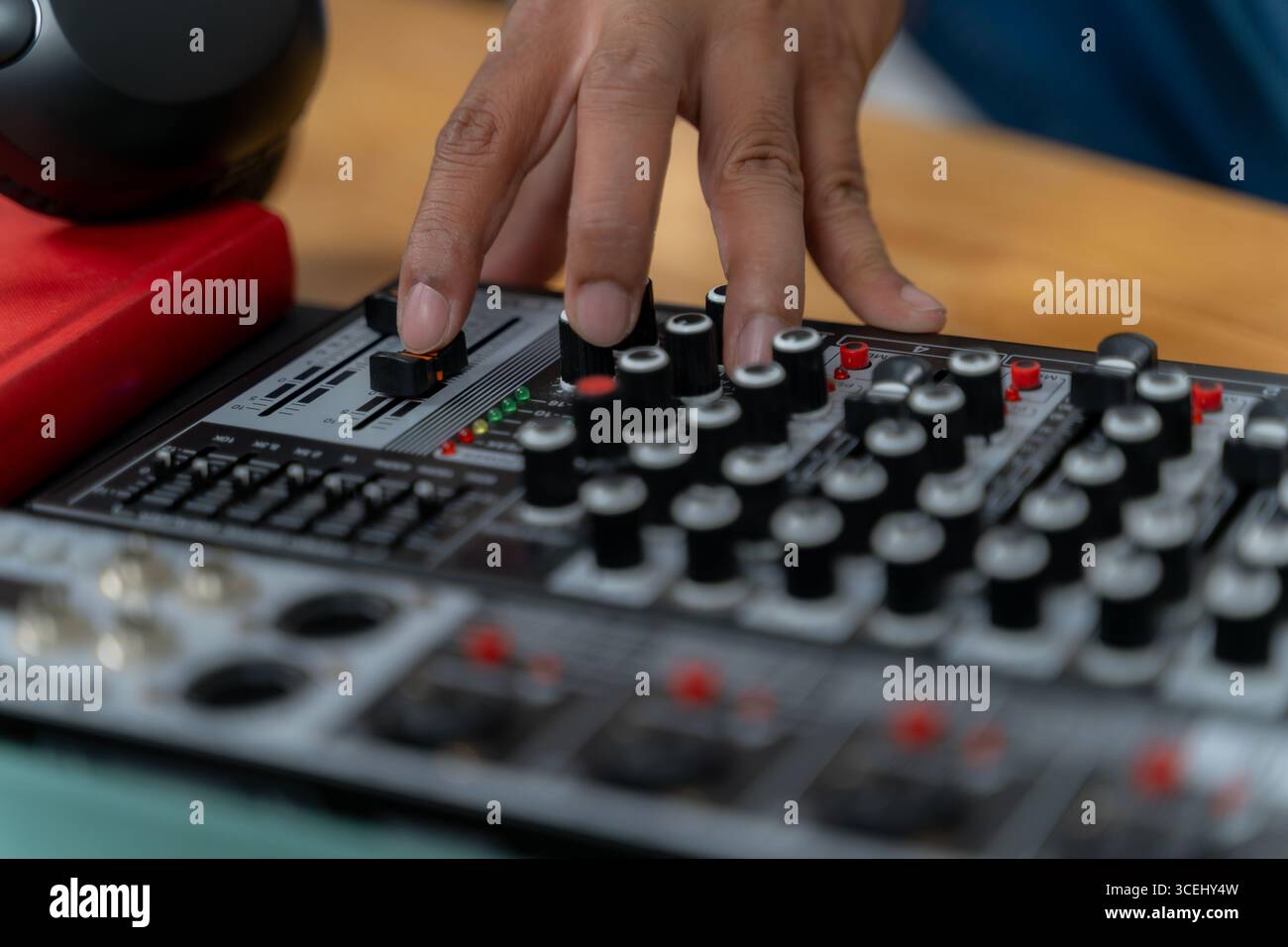 Eine Nahaufnahme einer Hand, die den Geräuschpegel auf einem Audiomixer einstellt und somit Podcast-Aufnahme, Übertragung und moderne Audioproduktion symbolisiert. Stockfoto