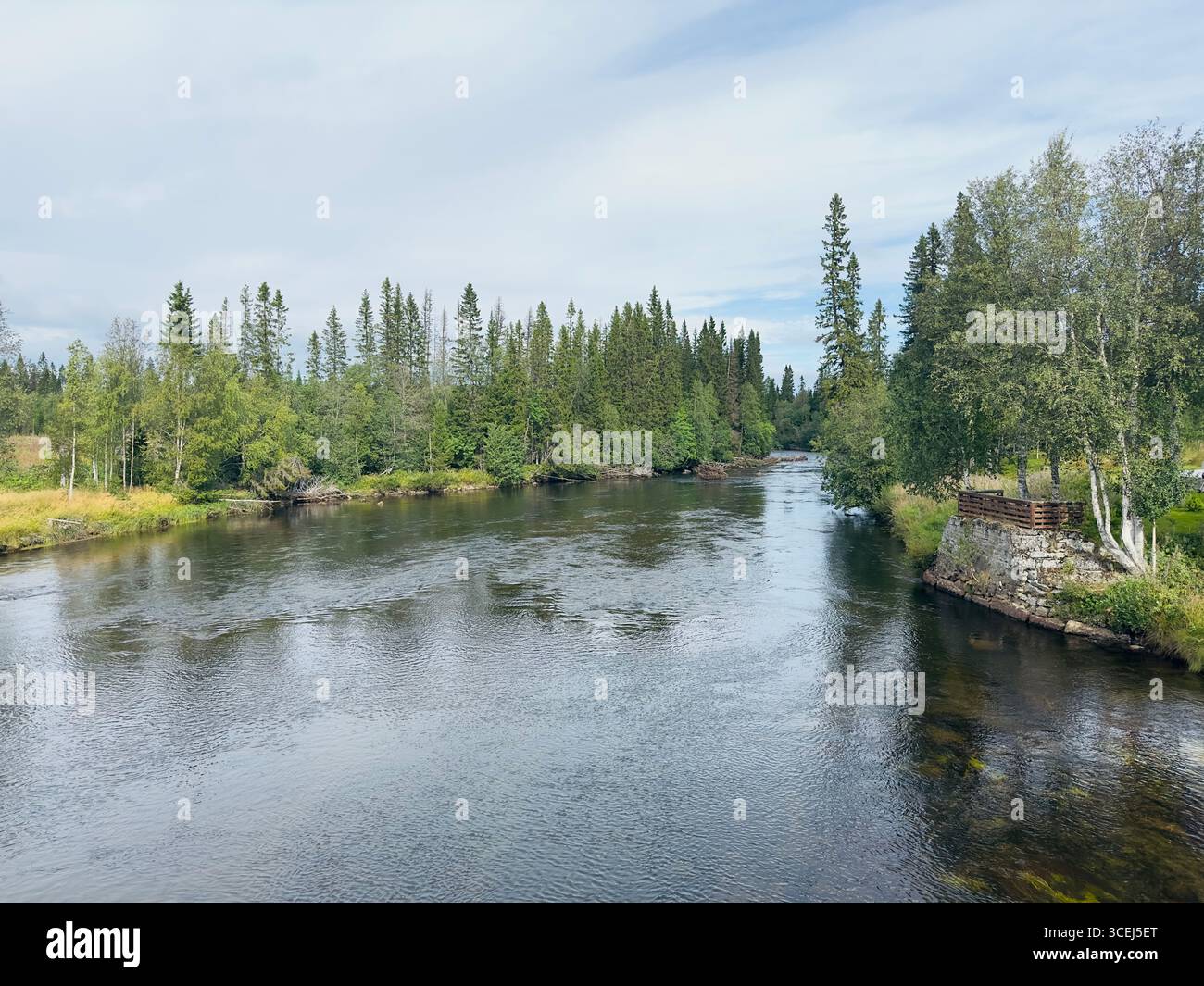 Eine rote Hütte befindet sich friedlich am Fluss, umgeben von üppigen grünen Bäumen und ruhigem Wasser. - Smartphone-aufgenommenes Stockfoto