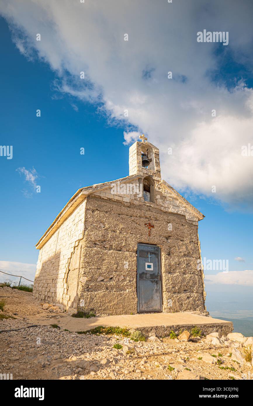 Steinkapelle auf Biokovo in der Nähe von Makarska Kroatien mit Glockenturm, felsiger Landschaft und dramatischen Wolken unter klarem Sommerhimmel Stockfoto