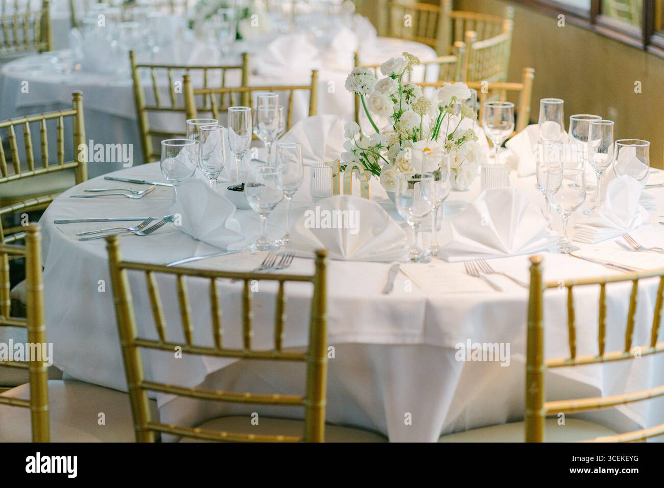 Runder Tisch mit weißer Bettwäsche und Blumenarrangements für eine formelle Zusammenkunft in einem Bankettsaal. Stockfoto