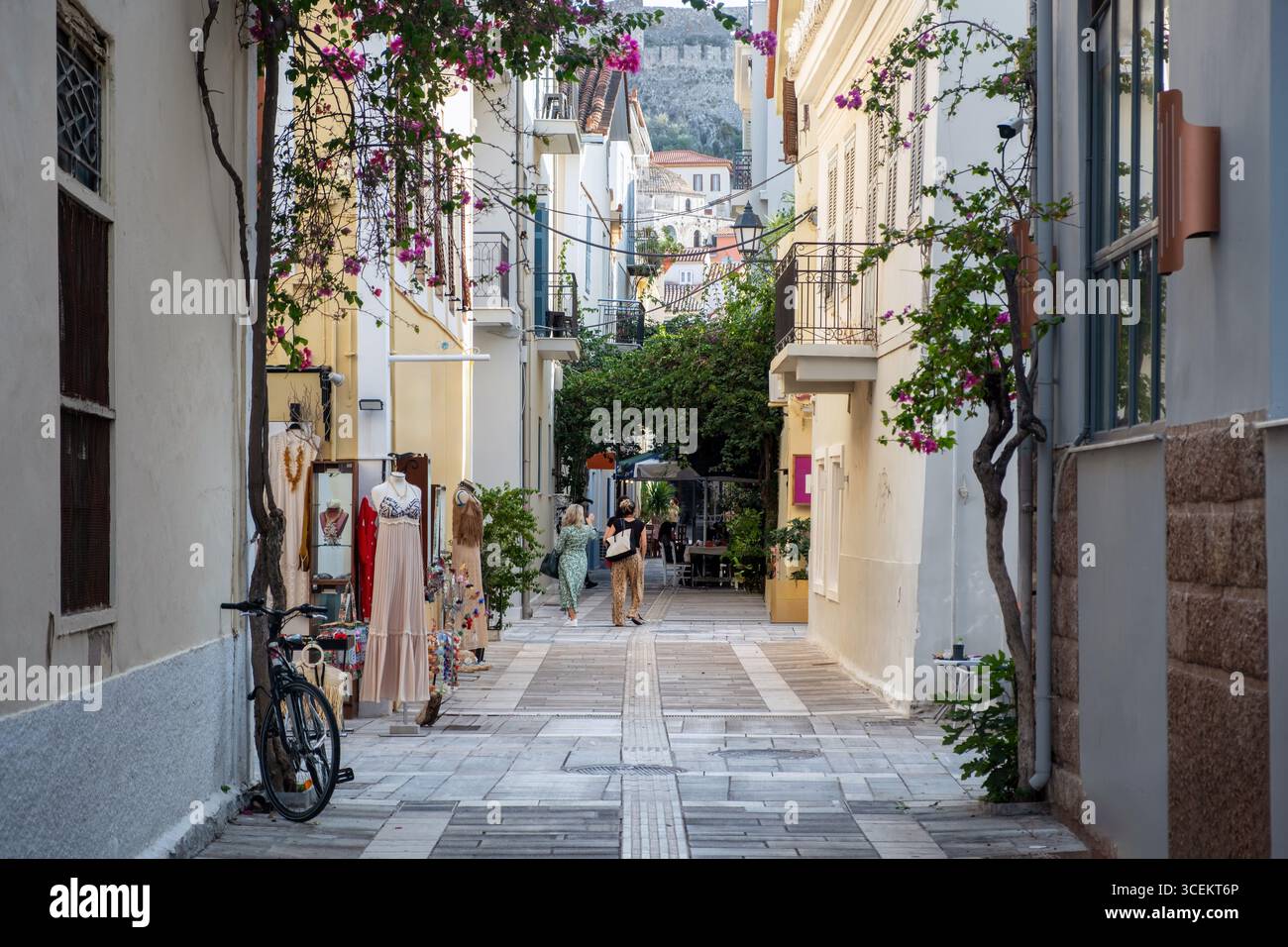 Malerische, enge Straße in Nafplio, Griechenland, gesäumt von kleinen Geschäften, blühenden Blumen und Balkonen, auf denen man gemütlich spazieren gehen kann Stockfoto