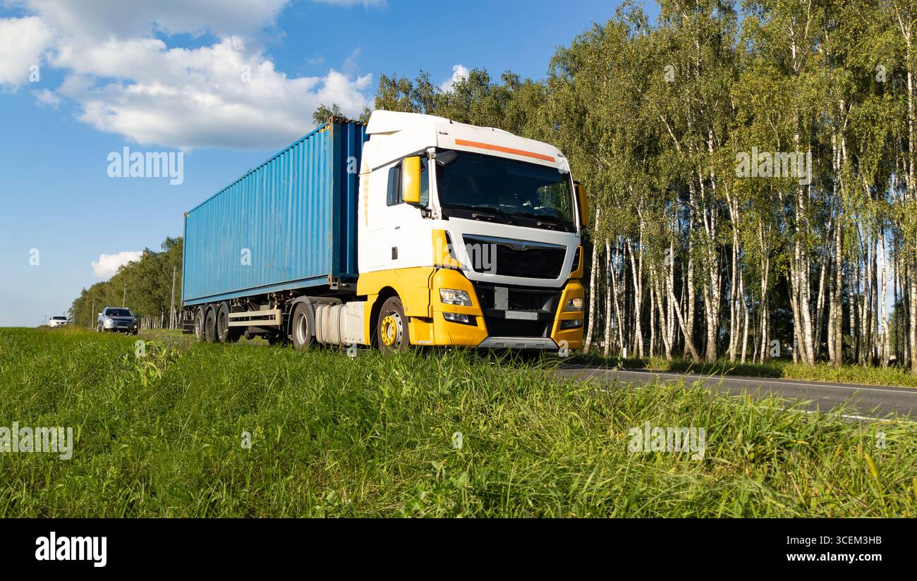 Großer Truck, der auf einer Landstraße in Bewegung gegen einen blauen Himmel und Wald fährt. Stockfoto