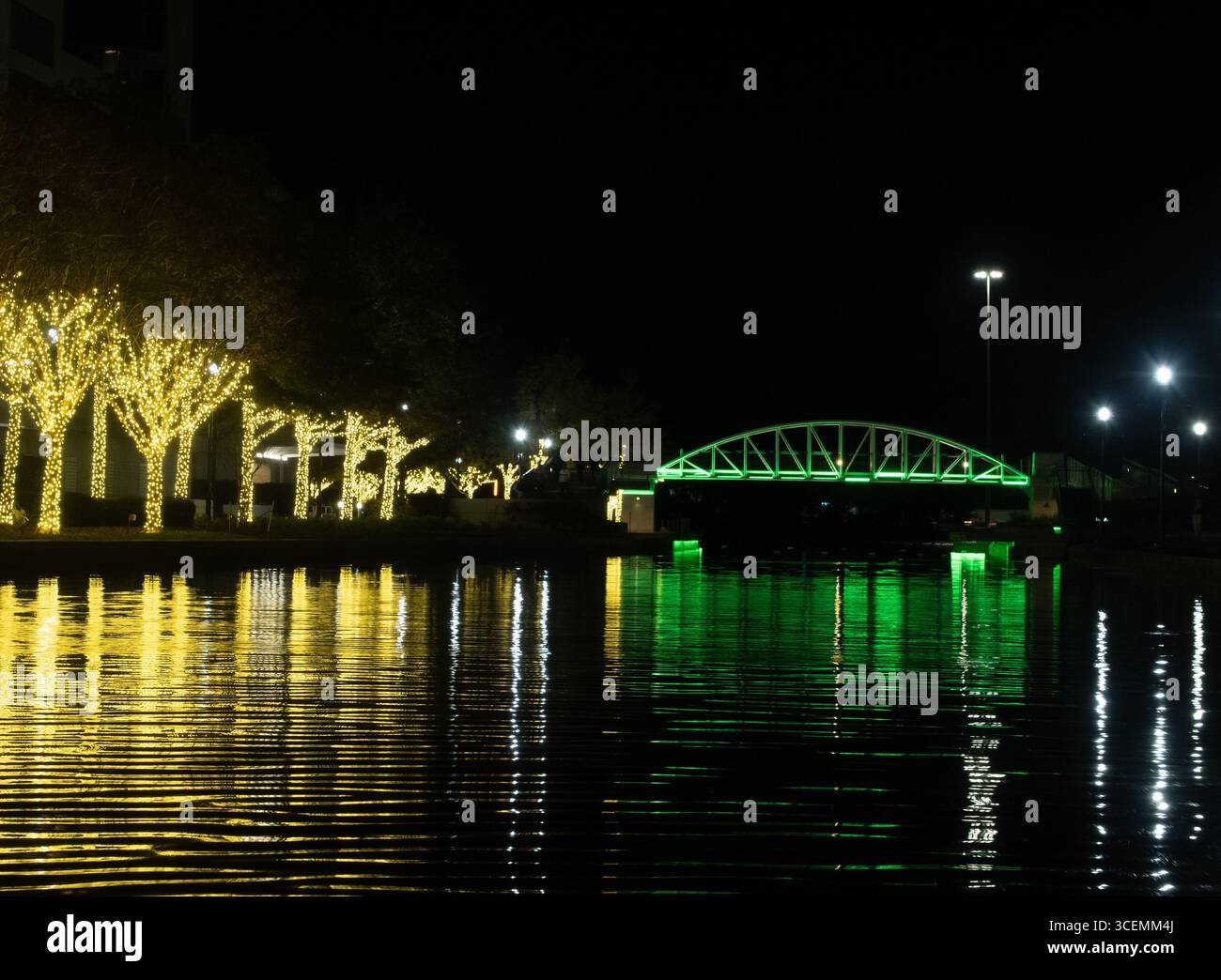 Bäume mit goldenen Lichtern und eine Brücke mit grünen Lichtern entlang des Waterway in den Woodlands, Texas. Vom Wasser aus fotografiert. Stockfoto