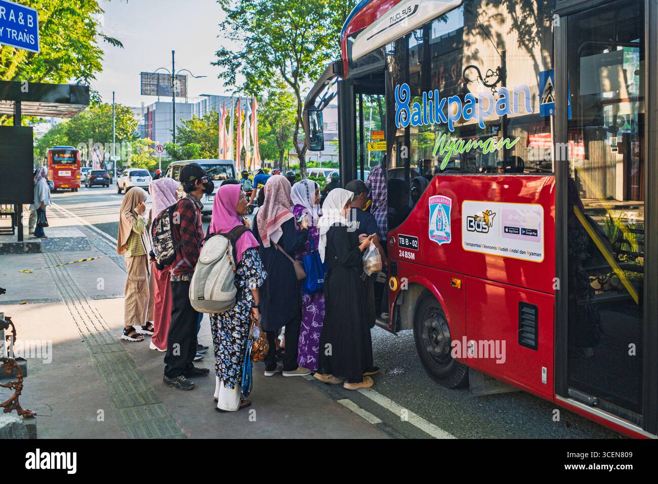 Balikpapan, Indonesien – 25. Juli 2025. Eine Gruppe von lokalen Pendlern, meist Frauen in Hijabs, die an einer Haltestelle von Trans Balikpapan in einen roten Stadtbus steigen Stockfoto