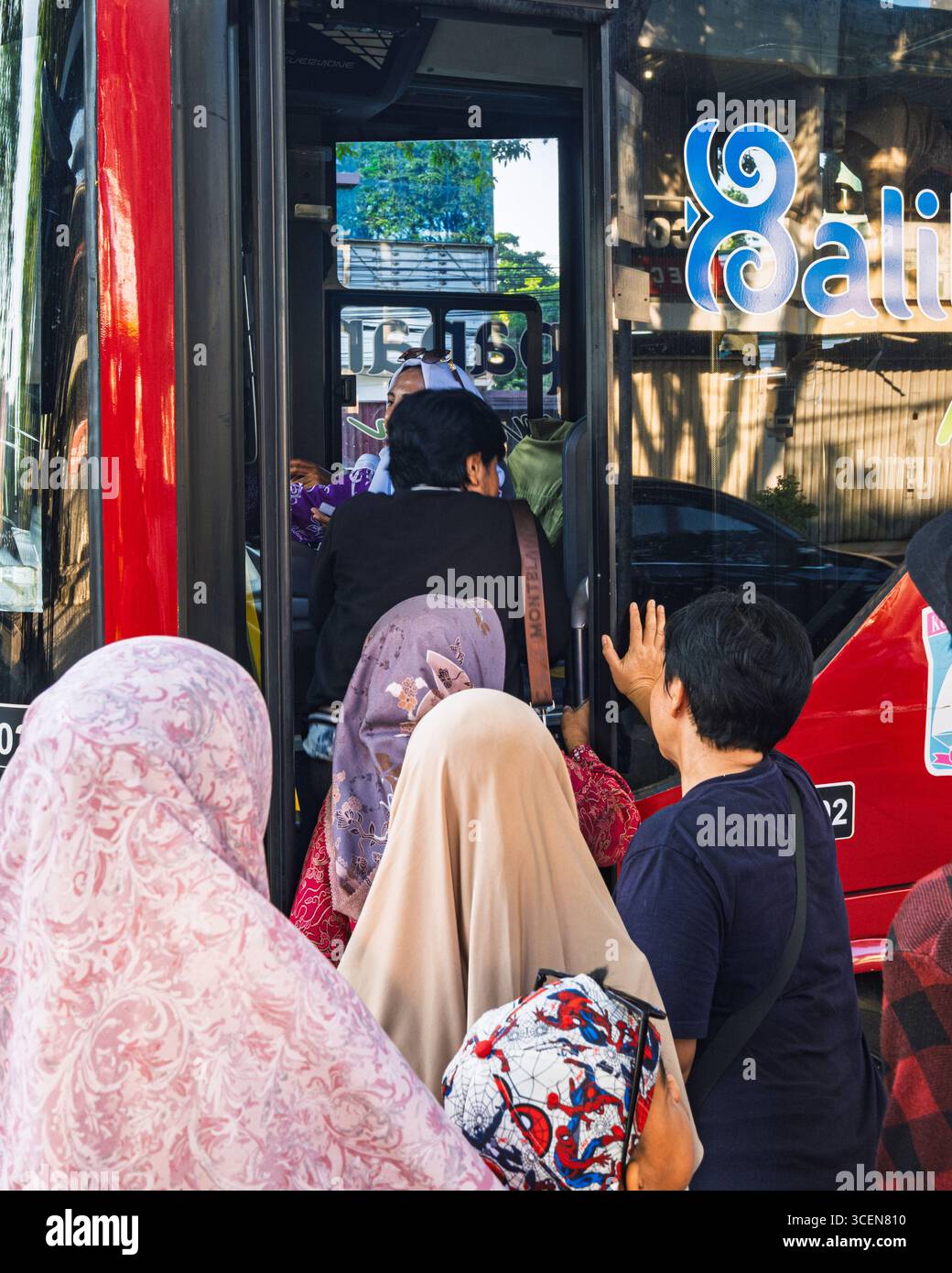 Balikpapan, Indonesien – 25. Juli 2025. Aus nächster Nähe sehen Sie Passagiere, einschließlich Frauen in Hijabs, die in einem roten Trans Balikpapan Stadtbus auf einem hellen Stockfoto