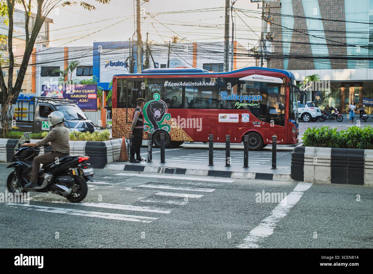 Balikpapan, Indonesien – 25. Juli 2025. Ein roter Trans Balikpapan Stadtbus fährt mit einem Verkehrsoffizier und Motorradfahrer durch eine geschäftige Straße Stockfoto