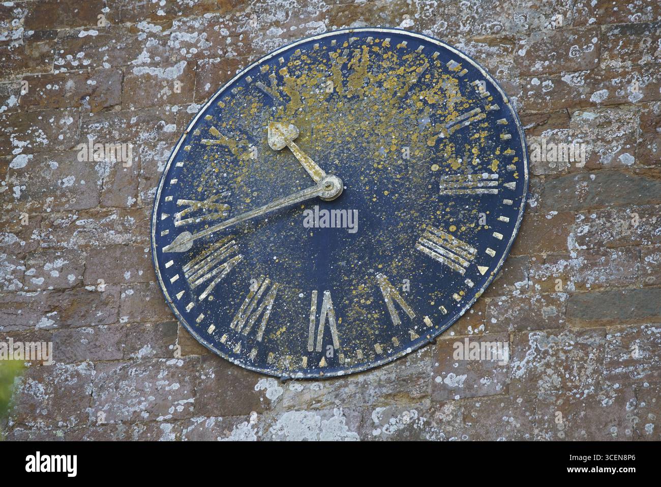Rustikale Uhr im Freien auf alter Steinmauer mit verwitterten römischen Ziffern. Deddington, England Stockfoto