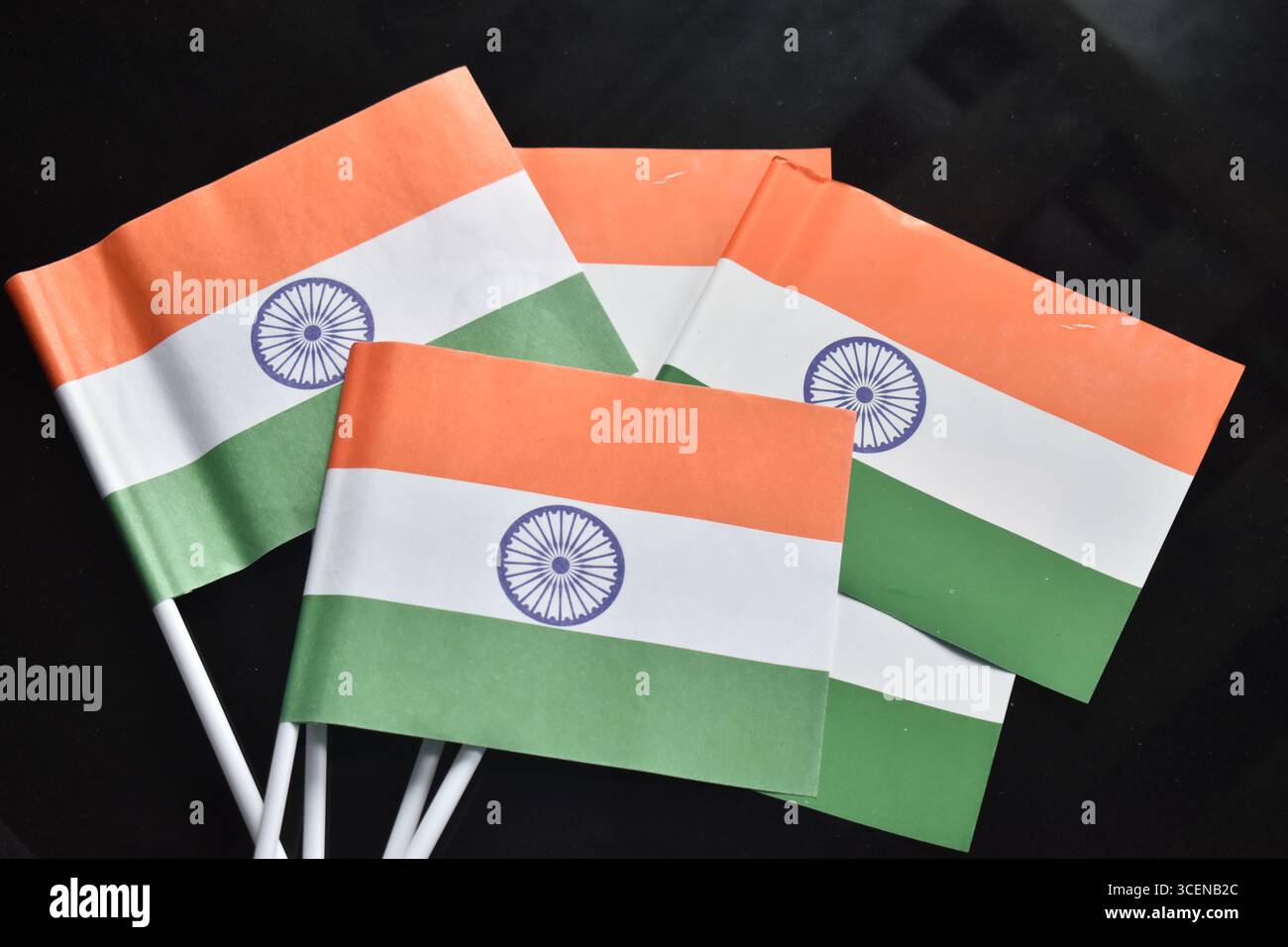 Eine Reihe kleiner indischer Nationalflaggen mit Safran-, weißen und grünen Streifen mit dem Ashoka Chakra, ordentlich auf dunklem Hintergrund angeordnet. Stockfoto