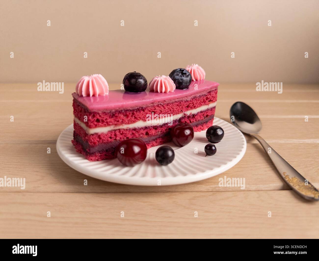 Appetitliche Scheibe rosafarbener Kuchen mit Sahnefüllung, garniert mit Heidelbeeren und Kirschen, serviert auf einem weißen Teller mit einem Löffel. Perfektes Dessert ph Stockfoto