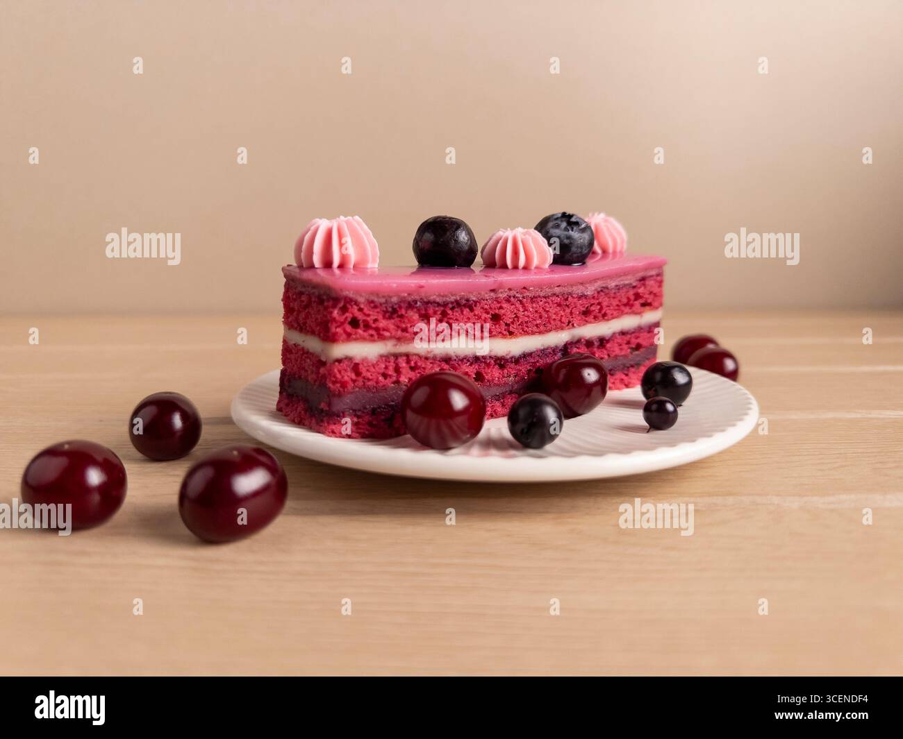Appetitliches Stück Kirsch- und Heidelbeerkuchen mit rosa Zuckerguss, garniert mit Schlagsahne und frischen Beeren, präsentiert auf einem weißen Teller Agave Stockfoto