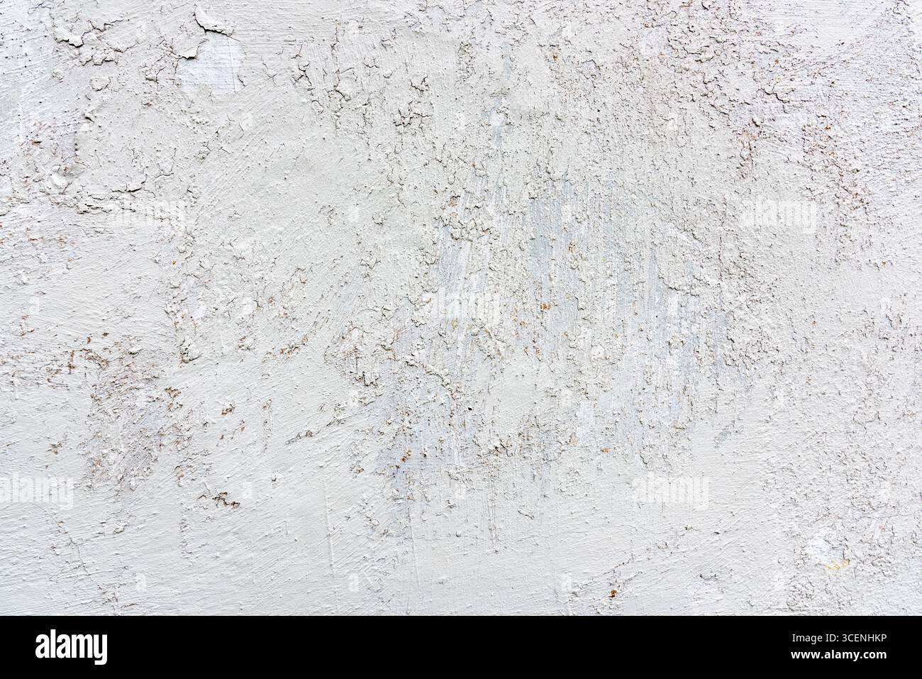 Eine strukturierte weiße Wand zeigt Gebrauchsspuren mit Rissen und Unregelmäßigkeiten, beleuchtet durch sanftes natürliches Licht in einer minimalistischen Umgebung. Stockfoto