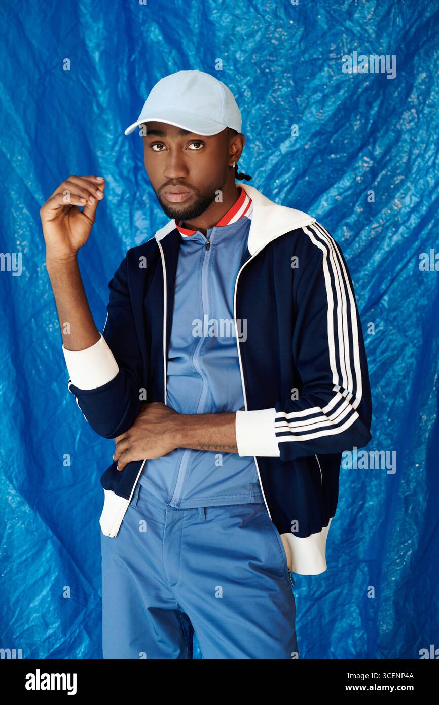 Ein gutaussehender junger Mann posiert selbstbewusst und präsentiert ein modernes Outfit vor einem auffälligen blauen Hintergrund. Stockfoto