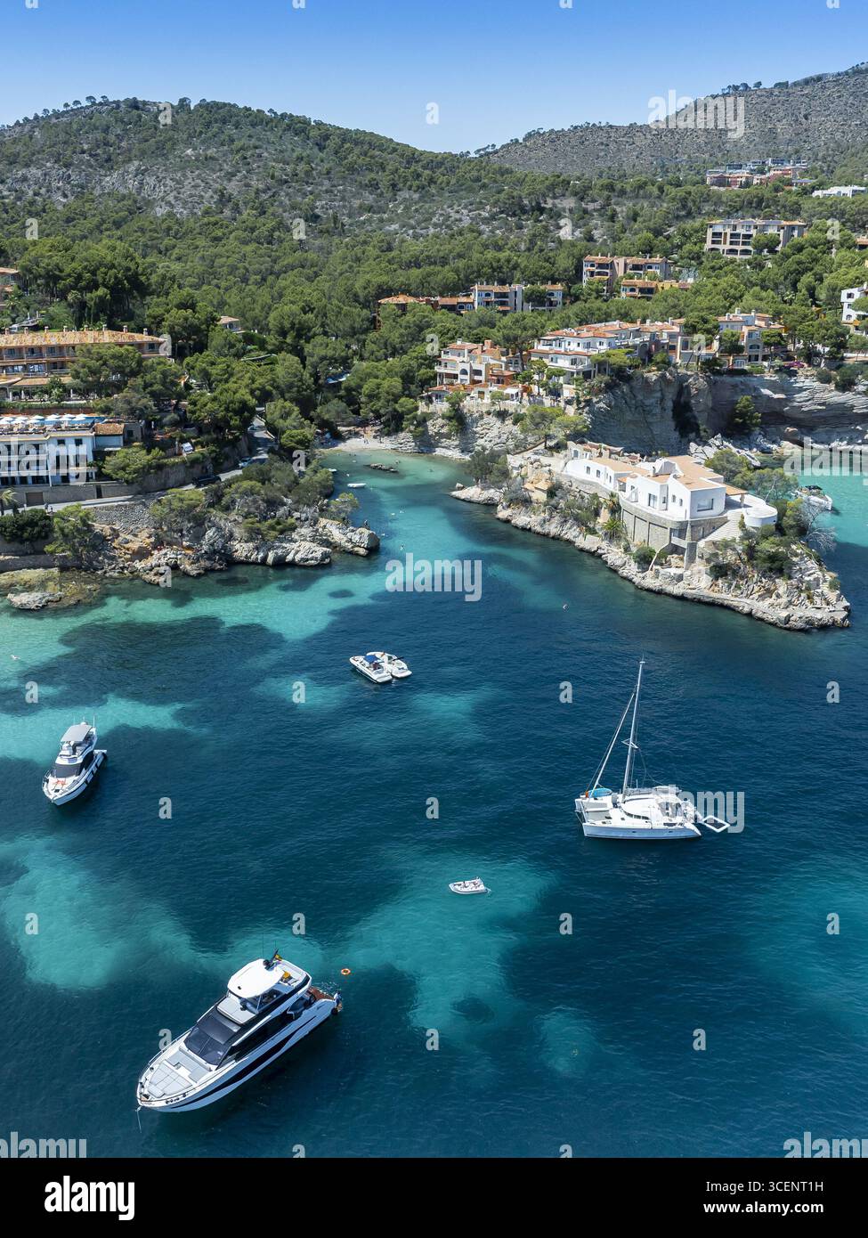 Blick aus der Vogelperspektive auf das lebhafte türkisfarbene Meer, das sanft die zerklüfteten Klippen und weiß getünchten Gebäude von Cala Fornells, Illes Balears, Spanien umschließt. Stockfoto
