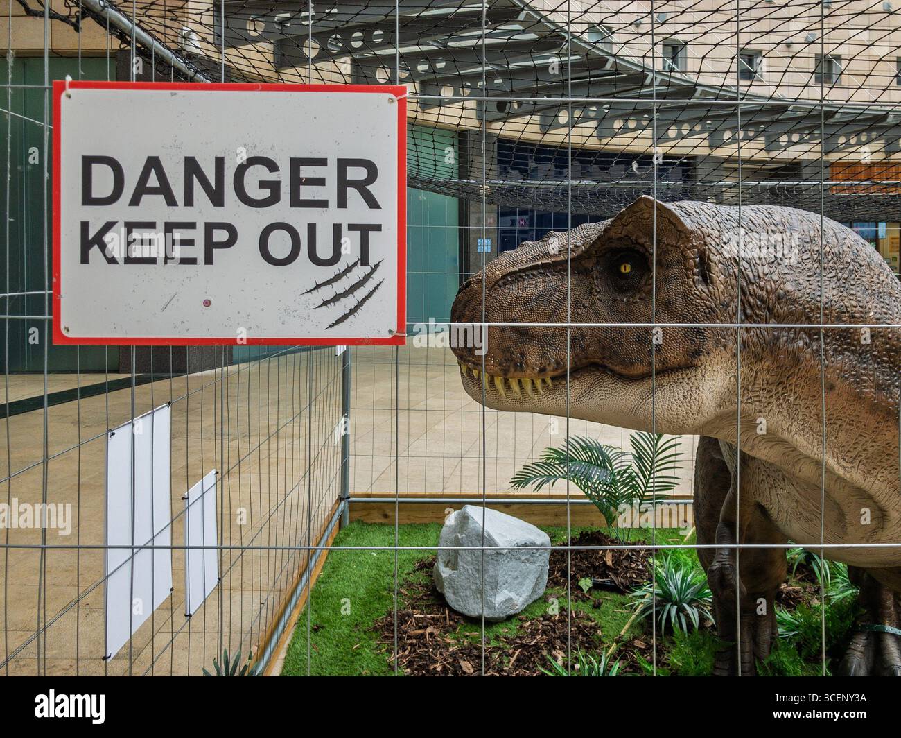 Lifesize-Modell Dinosaurier in einem Käfig mit Gefahrenhinweis; Teil eines Dino Discovery Events, Midsummer Place, Milton Keynes, Großbritannien Stockfoto