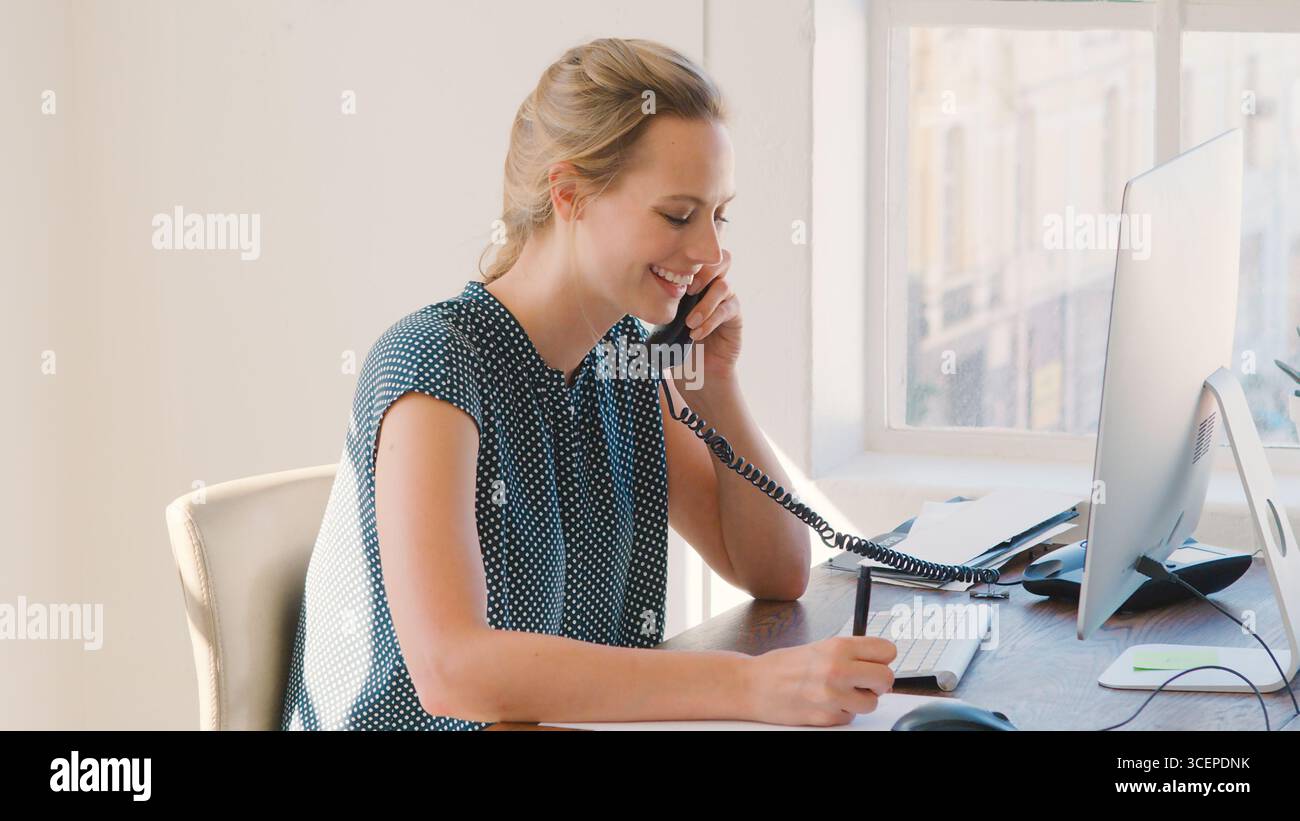 Junge Geschäftsfrau, Die Am Schreibtisch Am Computer Arbeitet Und Telefoniert Stockfoto