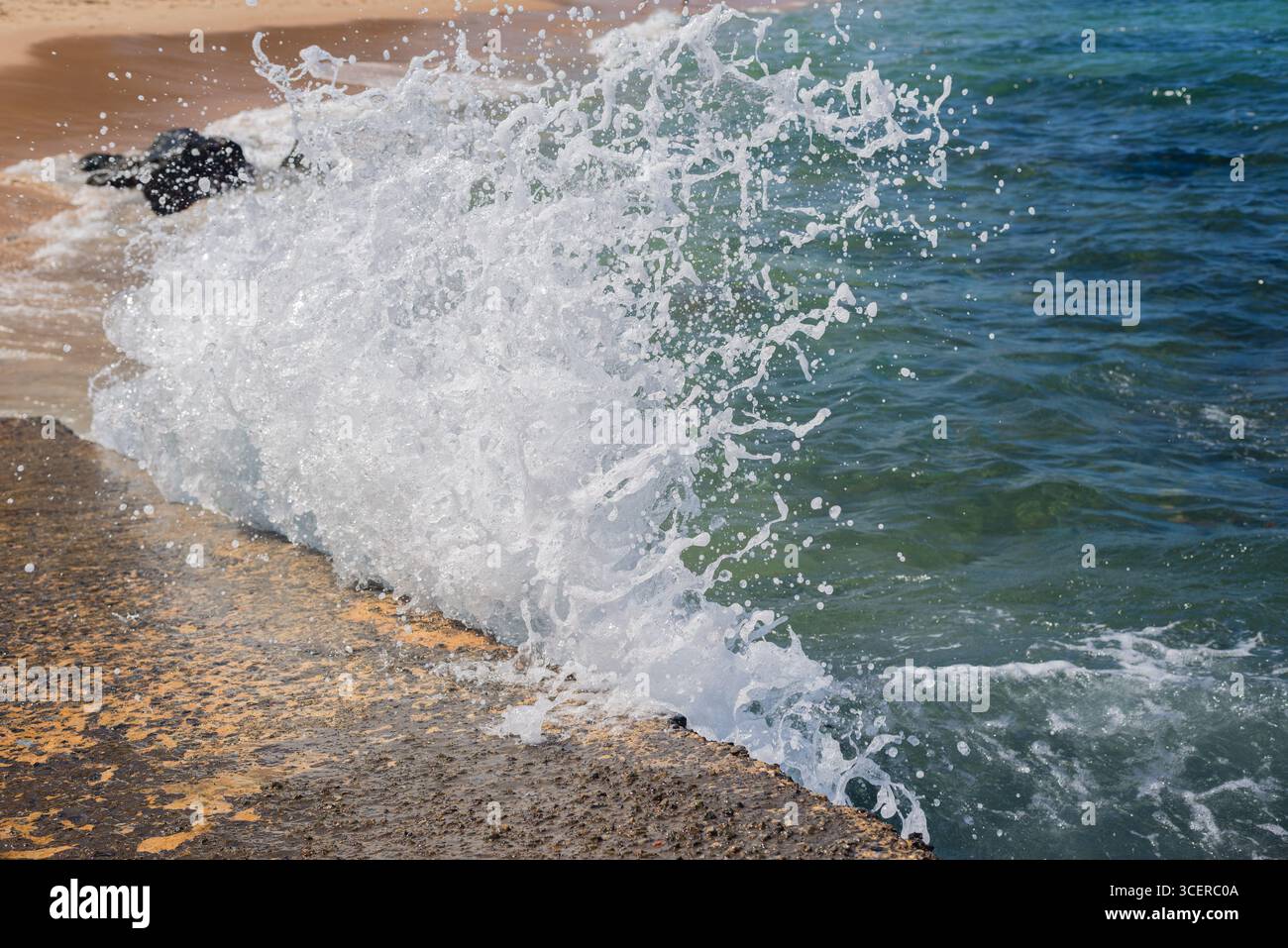 Spritzer einer Strandwelle, die hart gegen einen Zementpfeiler kracht. Wintersaison. Kraft der Natur. Stockfoto