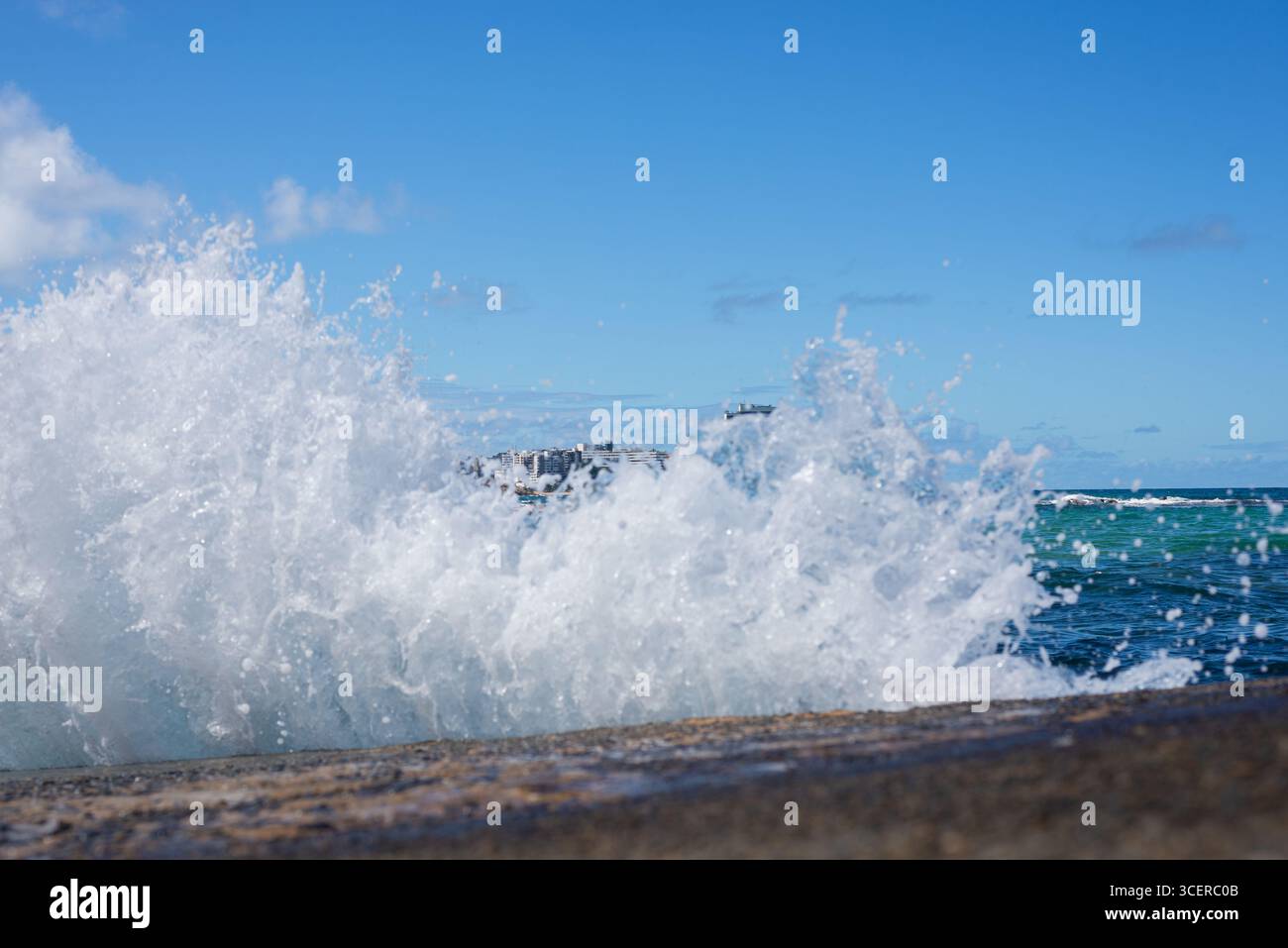 Spritzer einer Strandwelle, die hart gegen einen Zementpfeiler kracht. Wintersaison. Kraft der Natur. Stockfoto