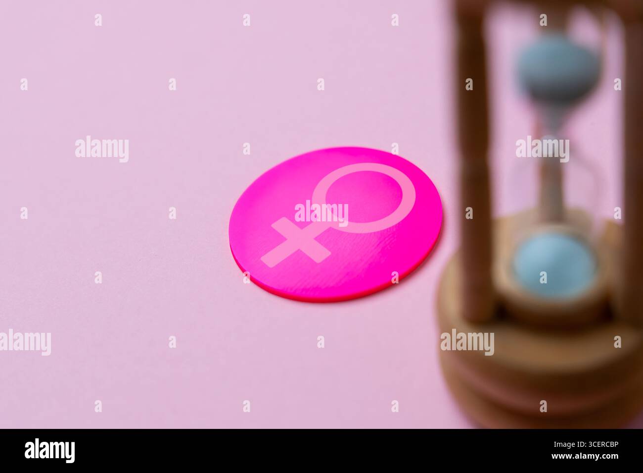 Eine hölzerne Sanduhr mit dem weiblichen Geschlechtssymbol. Frauengesundheit, Wechseljahre, Alterungskonzept. Kopierbereich für Text. Stockfoto