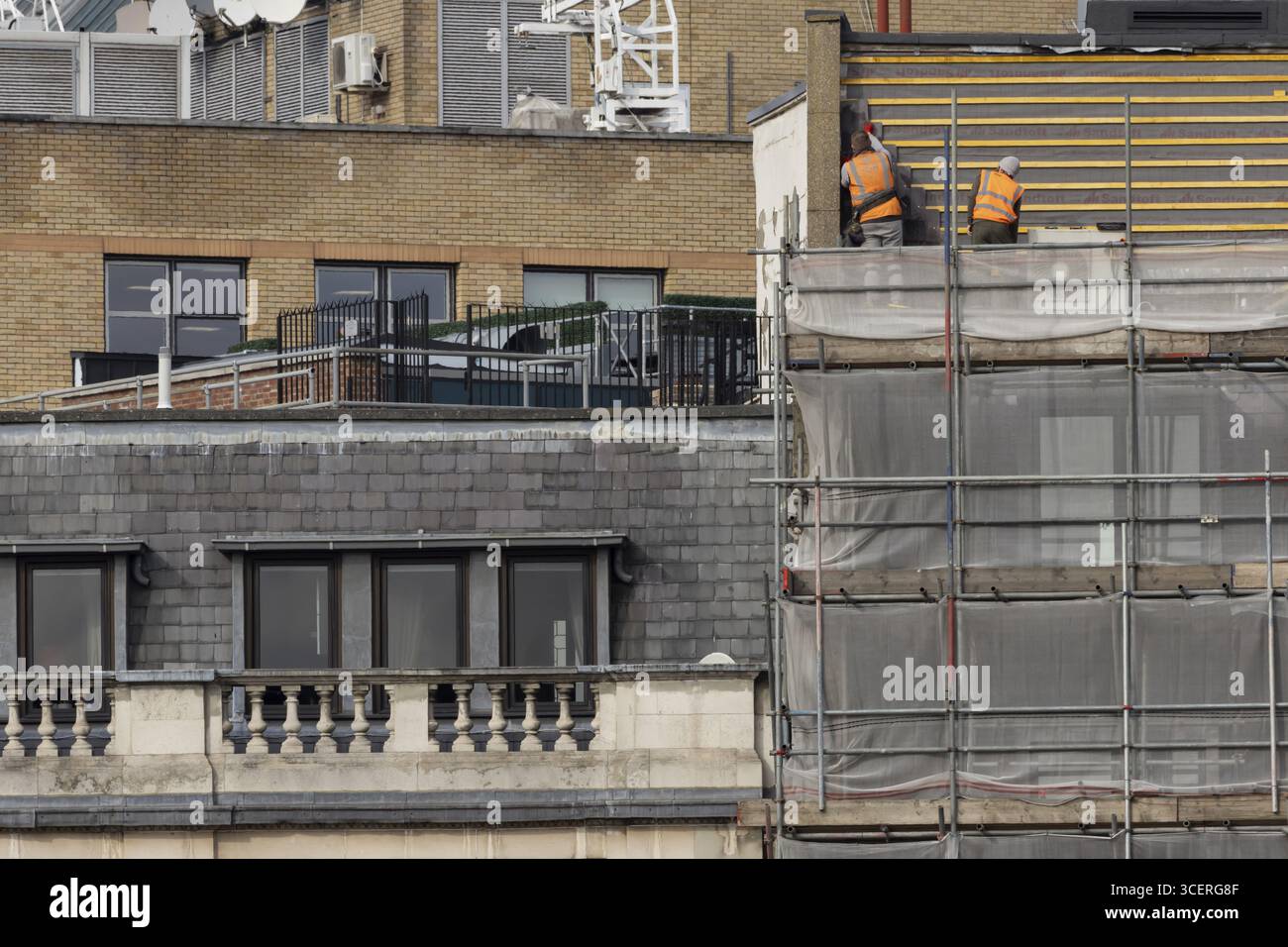 Zwei Arbeiter in hohen orangefarbenen Jacken auf Gerüsten in einem Gebäude in London, England, Großbritannien Stockfoto
