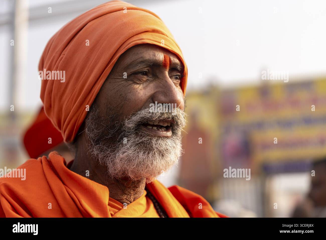 Indischer Sadhu in orangefarbenen Kleidern, der in die Ferne lächelt, Maha Kumbh Mela, Habeliya, Phulpur, Uttar Pradesh, Indien Stockfoto