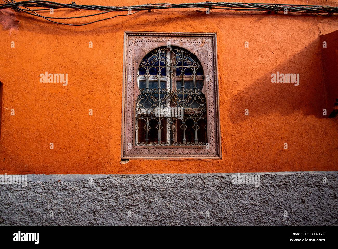 Dieses eindrucksvolle Foto zeigt ein wunderschön verziertes Fenster vor einer leuchtenden orangefarbenen Wand. Der aufwändig gestaltete Holzfensterrahmen zeigt Stockfoto