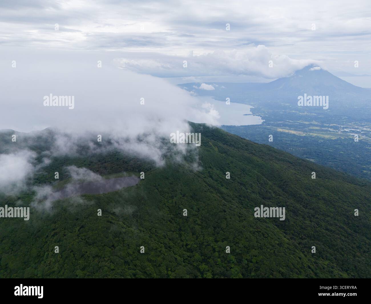 Der atemberaubende vulkanische Berg erhebt sich aus dichten Wolken und überblickt den ruhigen See bei Sonnenaufgang. Stockfoto