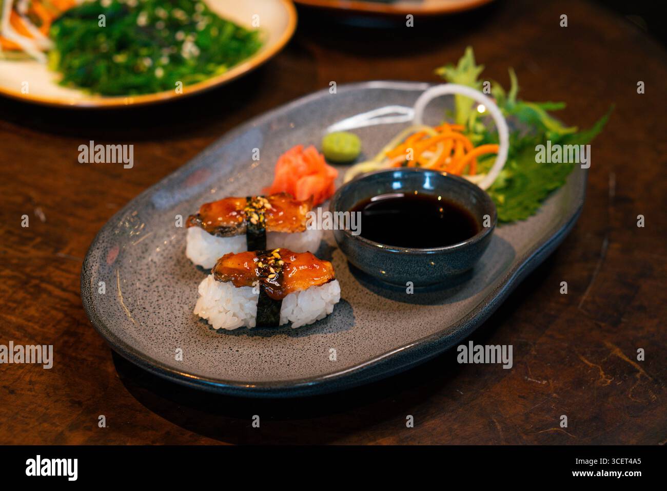 Frisches Unagi Nigiri Sushi serviert auf einem Teller mit Sojasauce und Gemüse Stockfoto