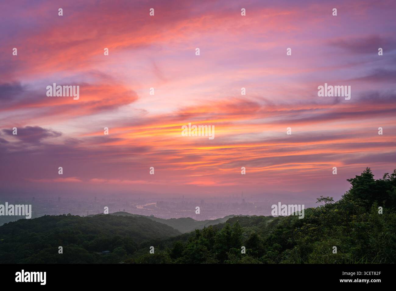 Ein großer Panoramablick auf Taipei City in der Abenddämmerung vom Dahan Mountain in New Taipei City, Taiwan, mit einem leuchtenden orangefarbenen Sonnenuntergangshimmel über dem fernen C Stockfoto