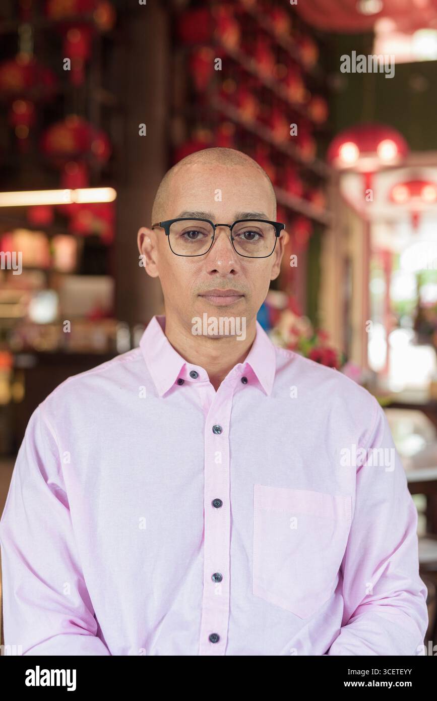 Glatze Hispanic reifer Mann in den 40er Jahren mit rosa lässigem Business-Shirt und Brille im chinesischen Teehaus-Restaurant. Kulturbegriff Relaxati Stockfoto