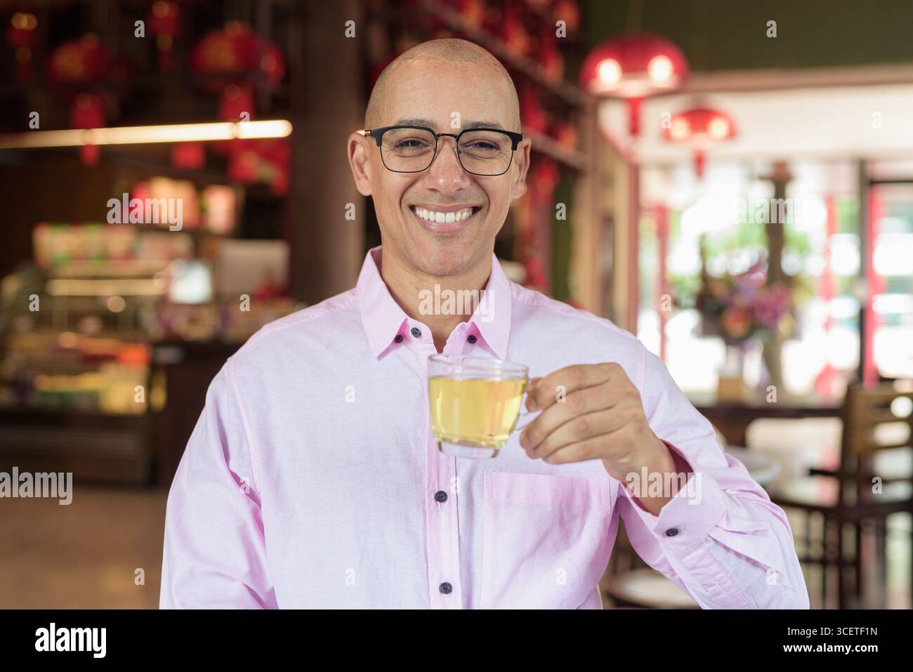 Glatze Hispanic reifer Mann in den 40er Jahren mit rosa lässigem Business-Shirt und Brille im chinesischen Teehaus-Restaurant. Kulturbegriff Relaxati Stockfoto