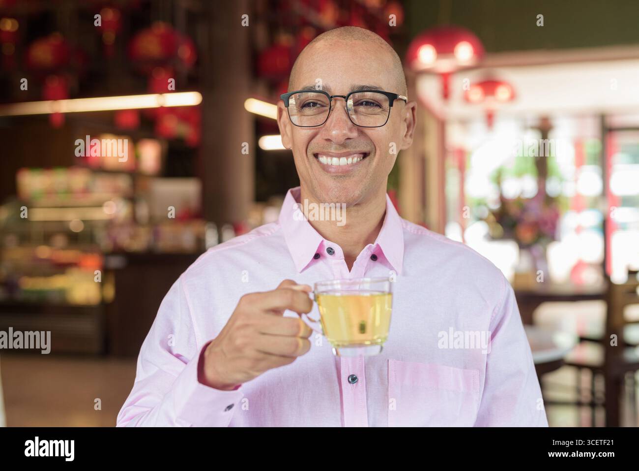 Glatze Hispanic reifer Mann in den 40er Jahren mit rosa lässigem Business-Shirt und Brille im chinesischen Teehaus-Restaurant. Kulturbegriff Relaxati Stockfoto