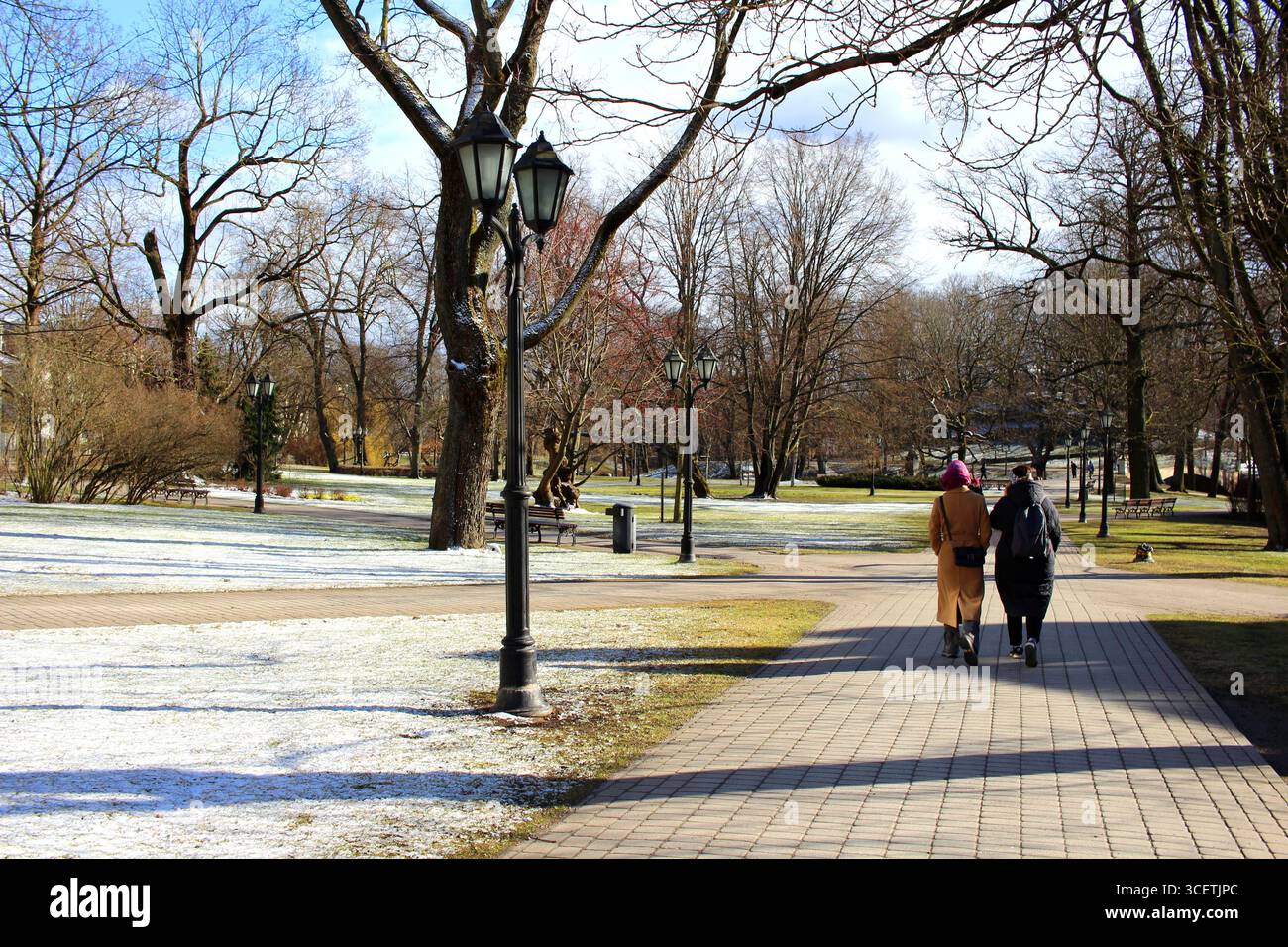 Zwei Personen laufen an einem sonnigen Tag durch einen frostigen Park - Bastejkalna Park, Riga, Lavia Stockfoto