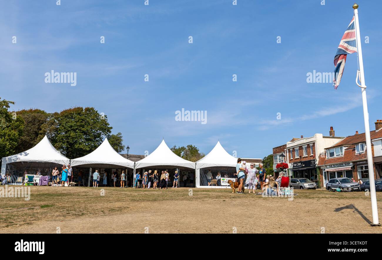 Menschen genießen einen sonnigen Tag bei Art on the Green Milford on Sea, einem Outdoor-Event mit weißen Zelten und britischer Flagge auf einem grasbewachsenen Feld mit Geschäften Stockfoto